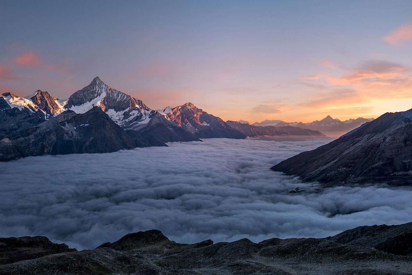 Sunrise over a sea of clouds surrounding snow-capped alpine peaks